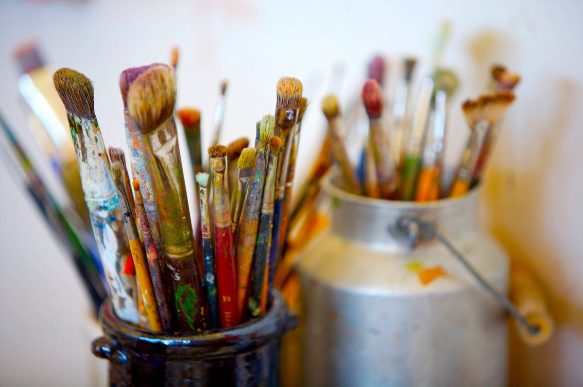 2 containers side by side filled with a large assortment of various shapes and sizes of paintbrushes.