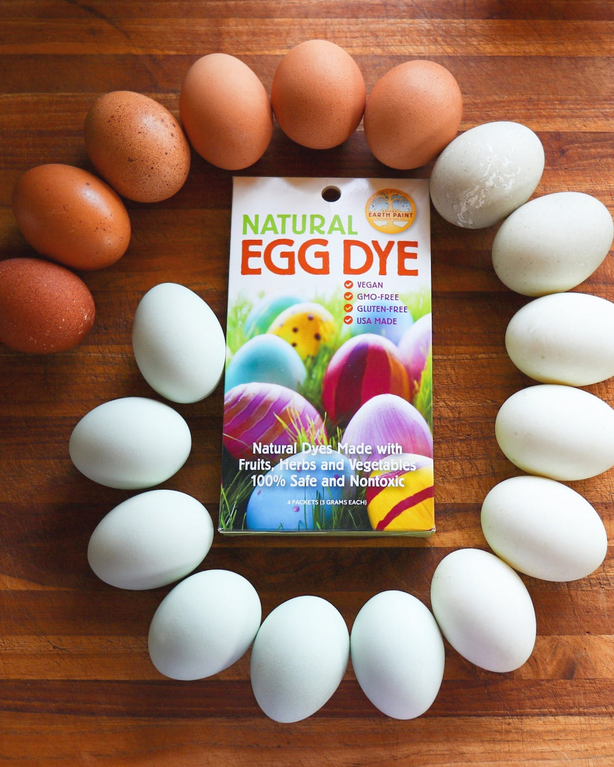 Spiral of eggs laid on a wooden table, encircling NEP's Natural Egg Dye Kit, ranging from colors white to brown