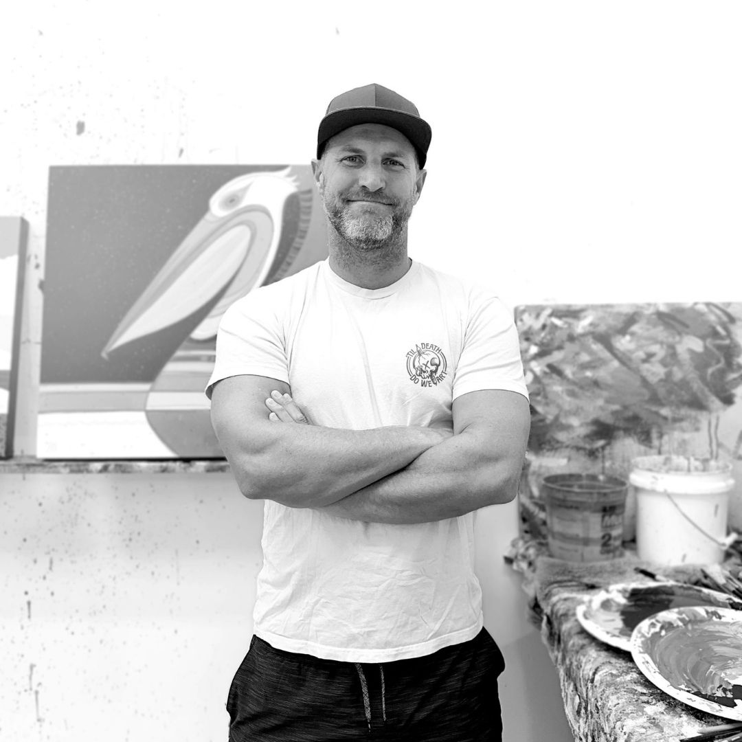 Man standing with arms crossed in front of a painting in his art studio