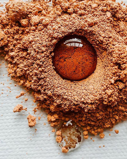 A drop of liquid nestled in a small pile of brown pigment on a glass palette