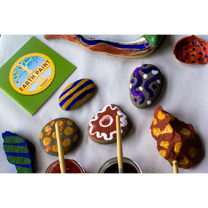 Samples of painted rocks, stones and wood with jars of paint and the Natural Earth Paint instruction booklet