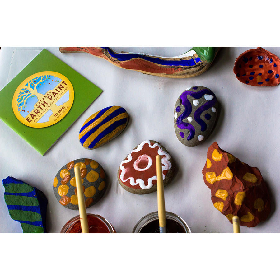Samples of painted rocks, stones and wood with jars of paint and the Natural Earth Paint instruction booklet