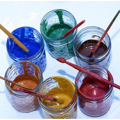 Six open jars of paint with paint brushes arranged in a circle