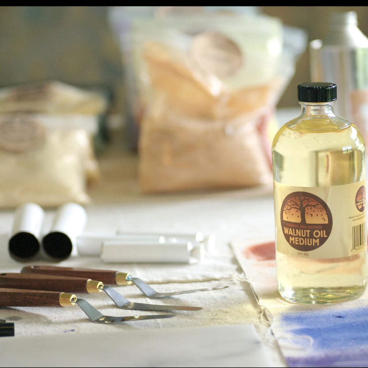 Various art supplies including the eight ounce bottle of walnut oil, three palette knives, unfilled paint tubes and plastic bags of pigment