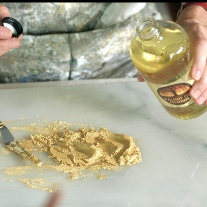 A lady about to add walnut oil to some gold pigment on a glass palette